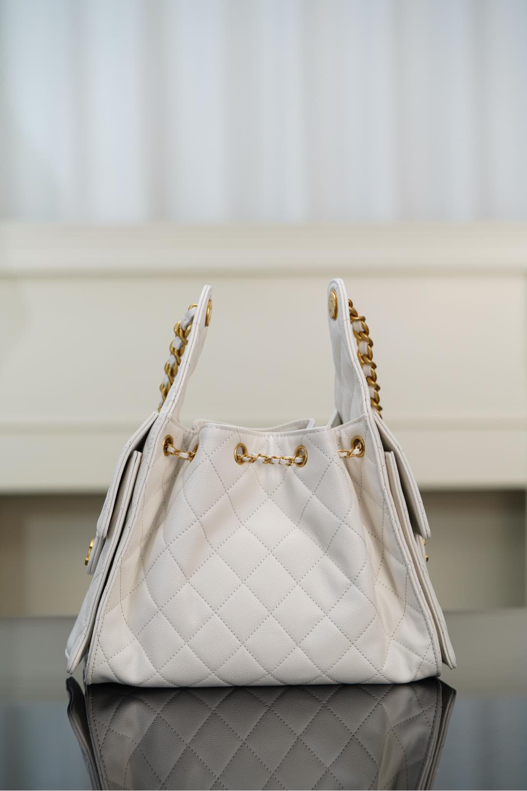 Chanel bag in white quilted leather with gold chain straps and side zipper pulls.