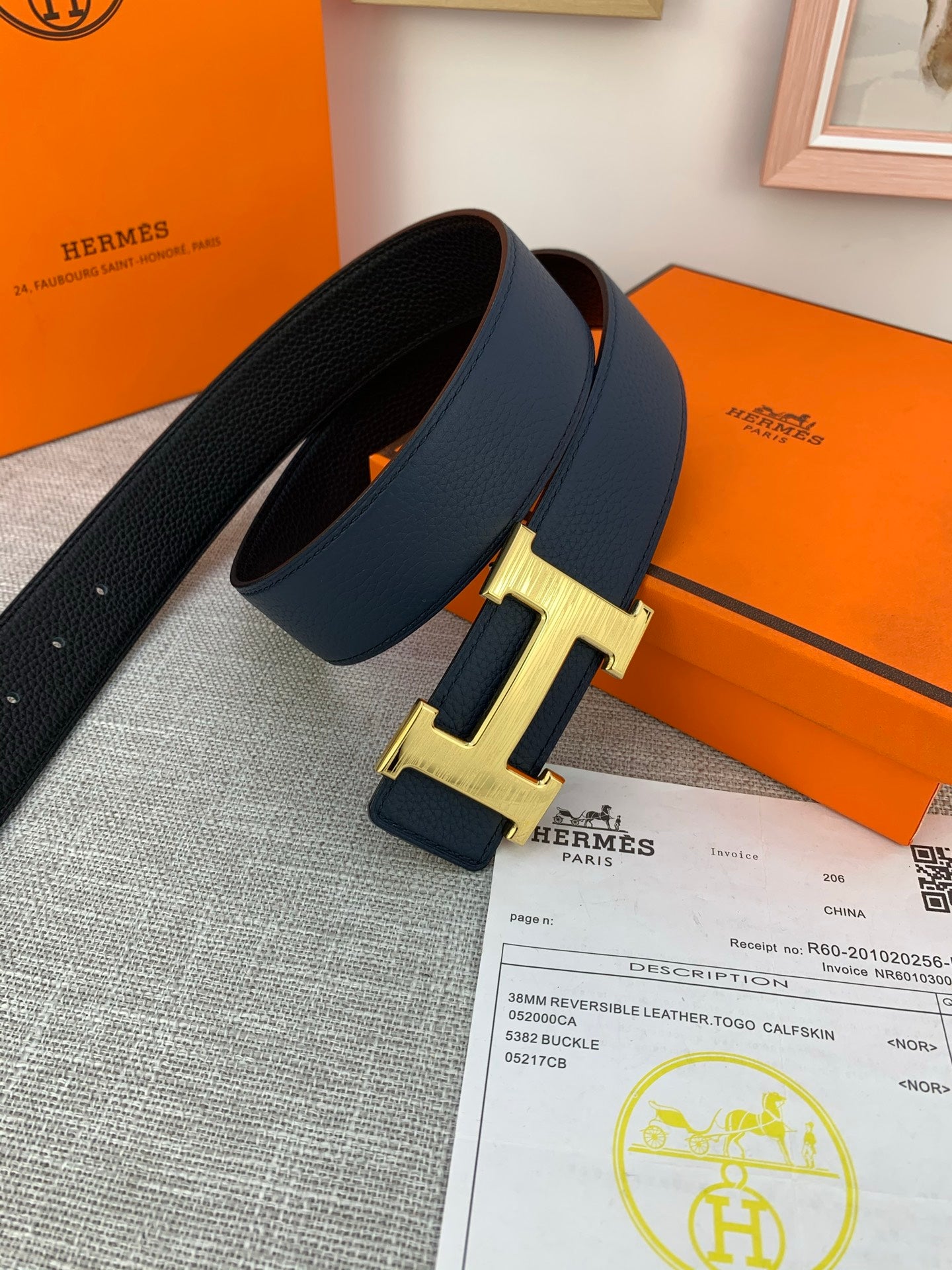 Hermes belt with navy leather strap and gold H buckle, photographed with paperwork