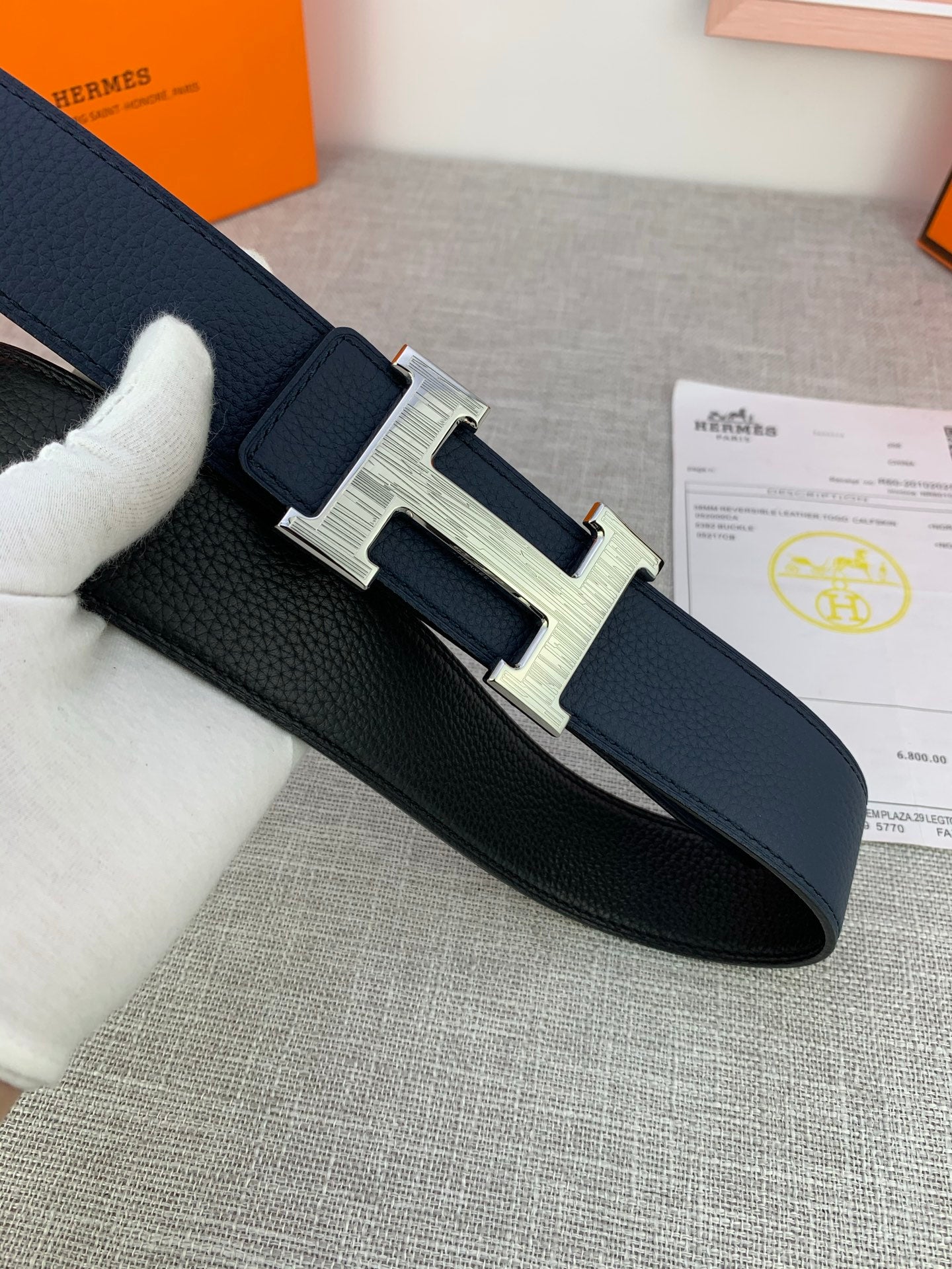 Hermes belt with navy leather strap and silver H buckle, side view with paperwork