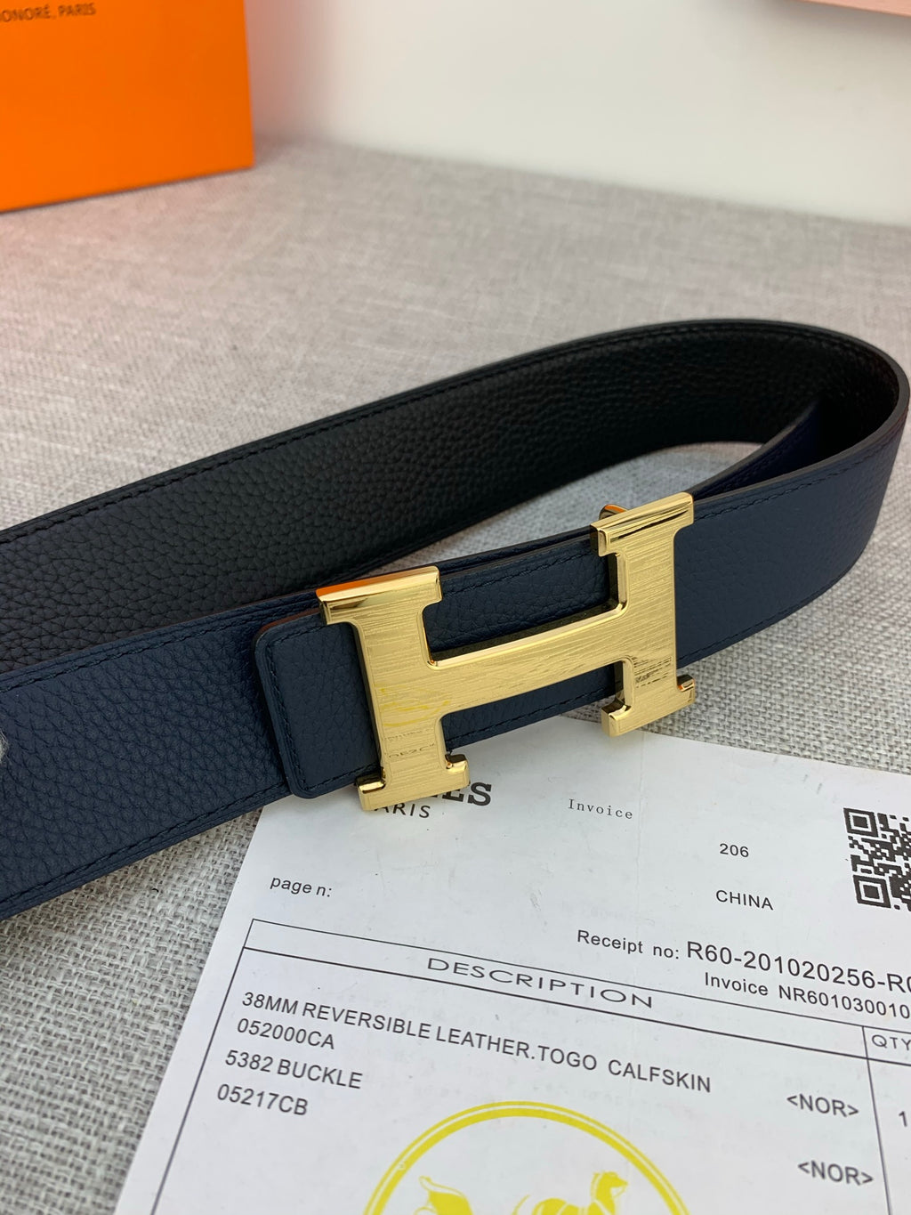 Hermes belt close-up with navy leather strap and gold H buckle, with receipt