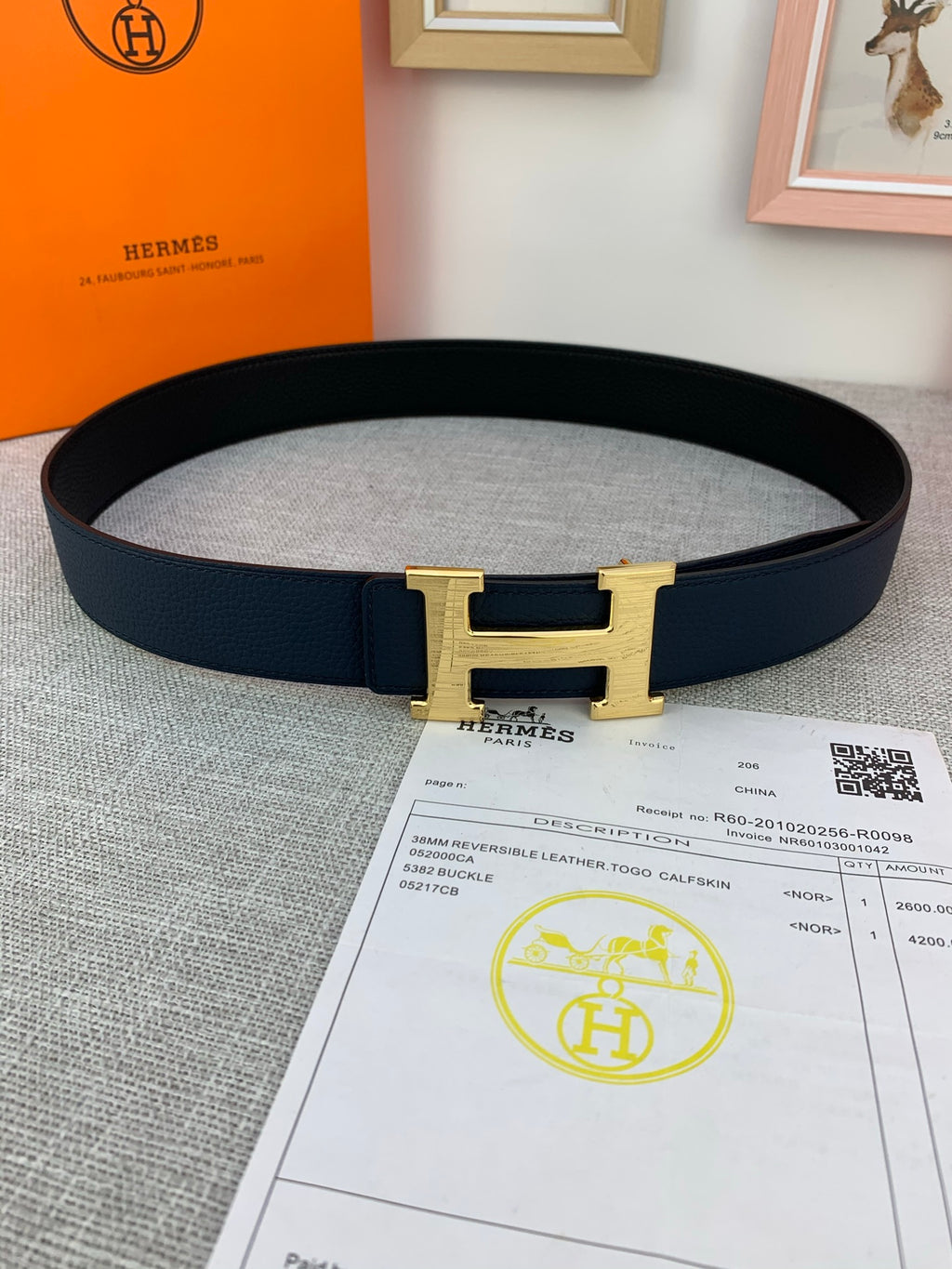 Hermes belt with navy leather strap and gold H buckle, laid flat with receipt