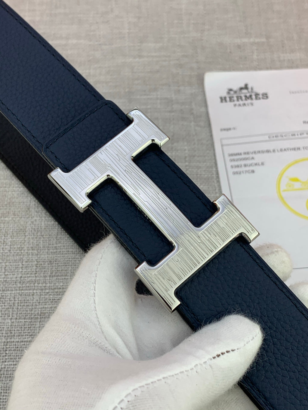Hermes belt close-up with navy leather and silver H buckle detail in hand