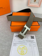 Reversible leather belt with olive strap and silver-tone H buckle in front of box