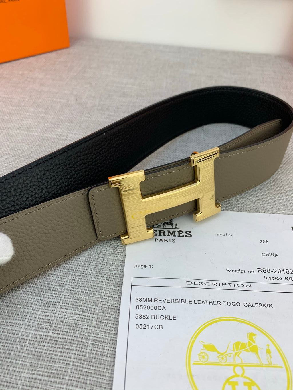 Reversible leather belt close-up showing olive strap, black side, and gold-tone H buckle