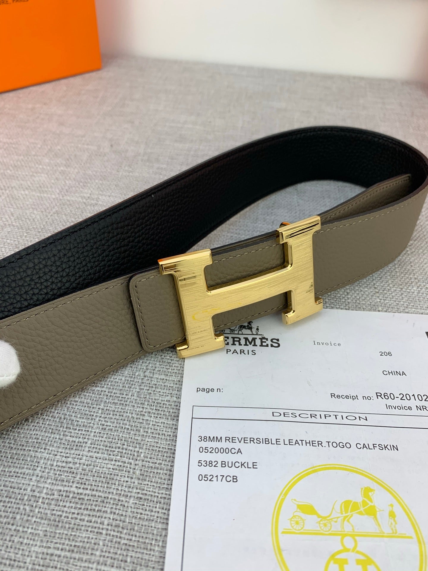 Reversible leather belt close-up showing olive strap, black side, and gold-tone H buckle