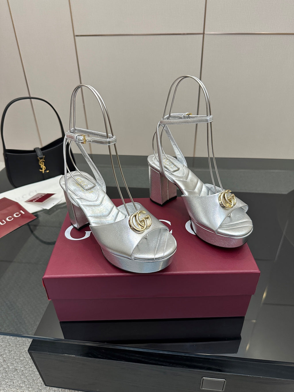 Pair of silver platform heeled sandals with gold logo emblem, open toe and ankle strap