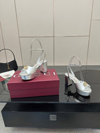 Silver open-toe platform sandals with gold logo emblem and slim straps, on shoe box