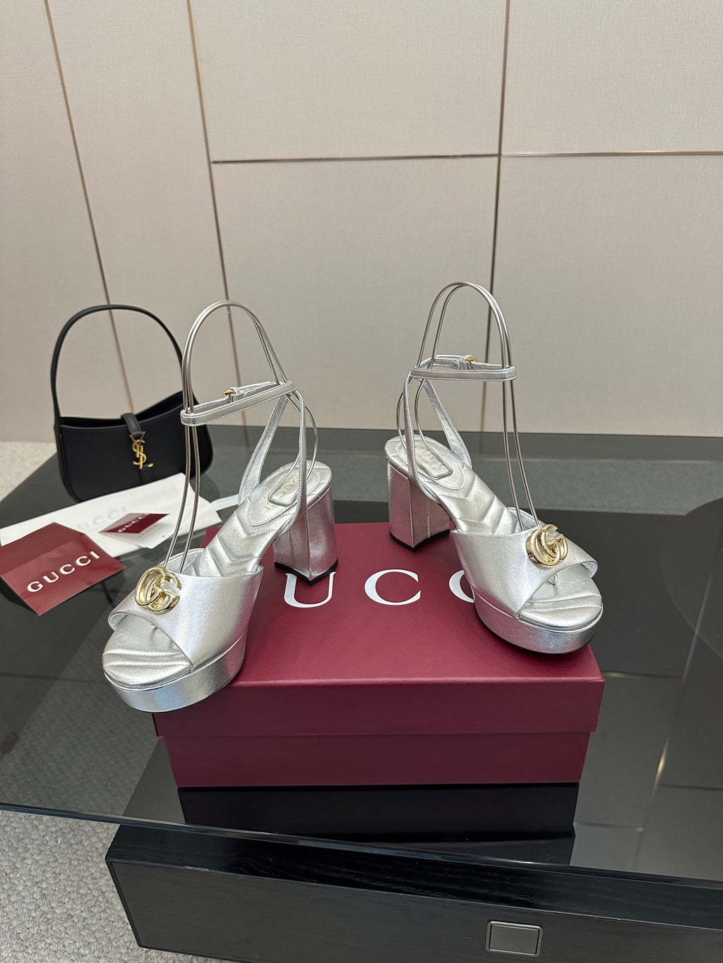 Silver open-toe platform sandals with gold logo hardware and tall slim heels, on display