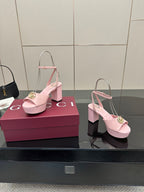 Pink heeled sandals with open toe, slingback straps, and gold logo buckle at front.