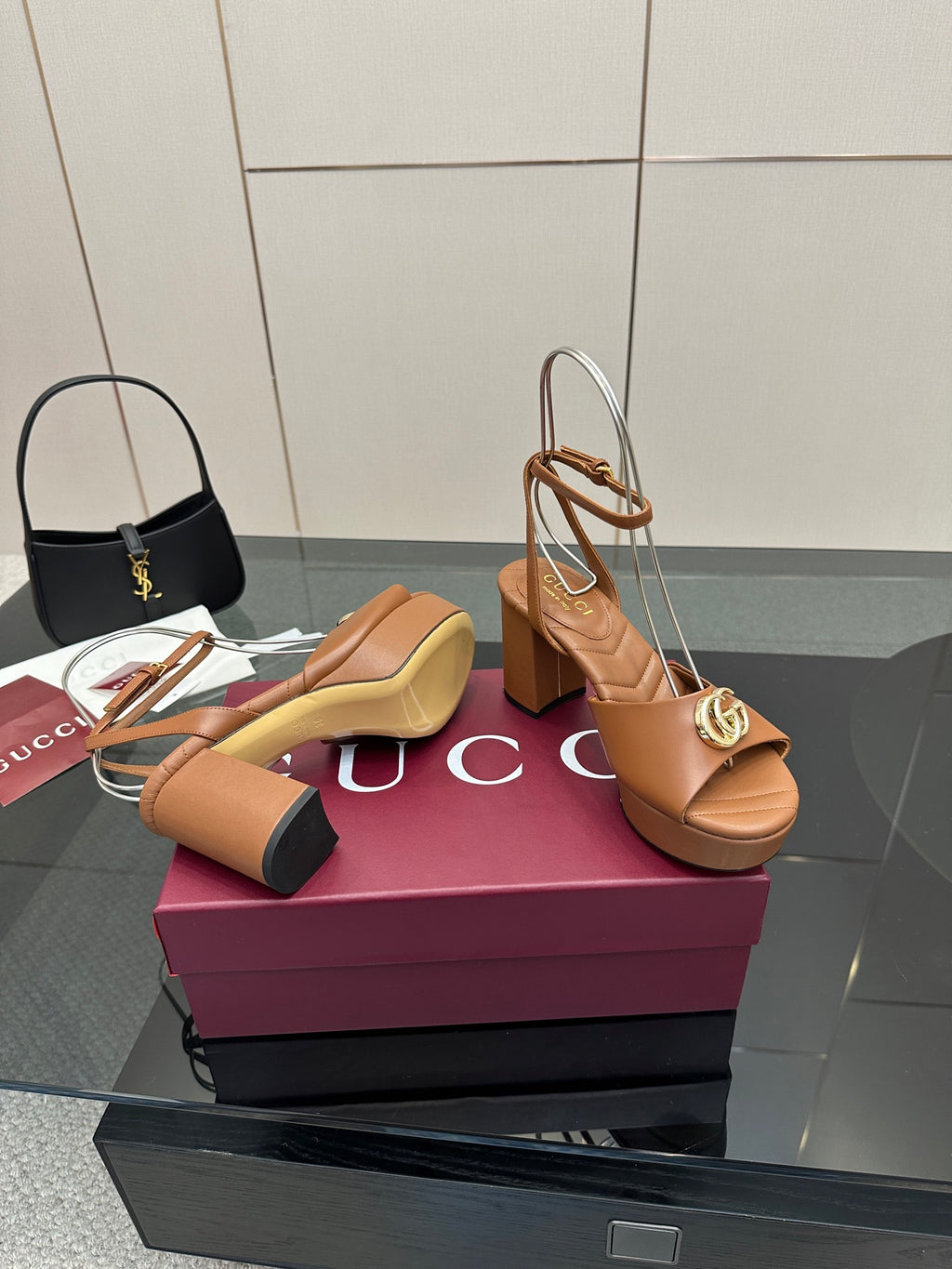 Tan heeled sandals with open toe, ankle strap, and gold GG buckle on platform heel