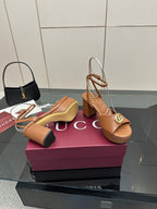 Tan heeled sandals with open toe, ankle strap, and gold GG buckle on platform heel
