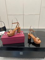 Tan open-toe heeled sandals with ankle strap and gold GG buckle, angled on box