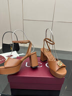Tan heeled sandals with open toe, ankle strap, and gold GG buckle on block heel