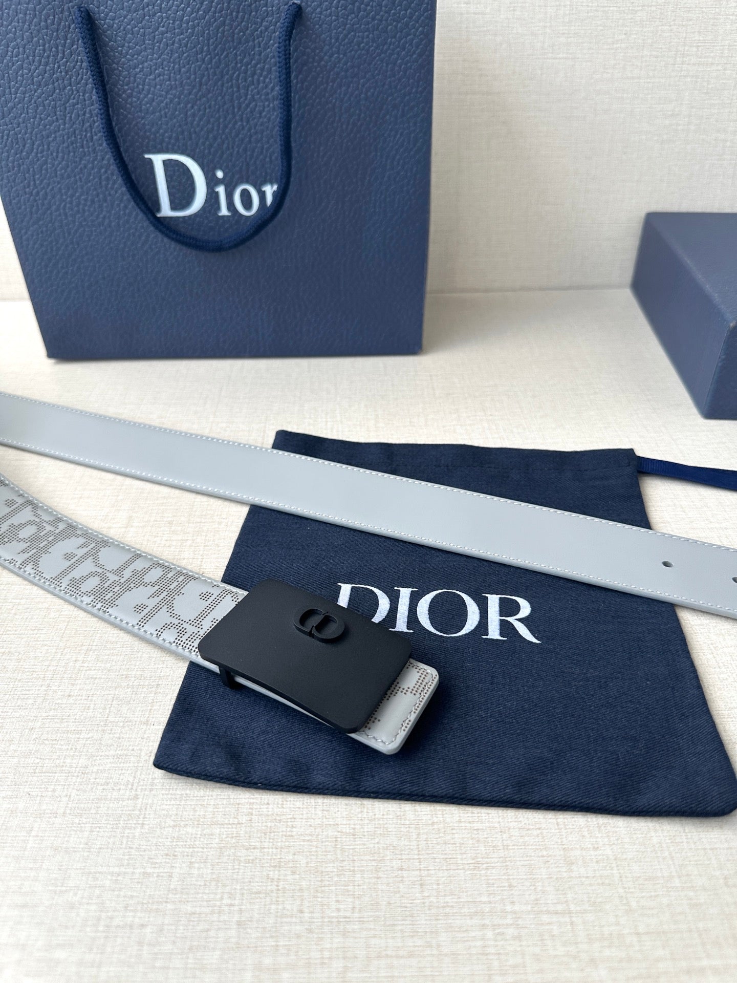 Dior belt strap laid flat: light gray pattern with navy buckle