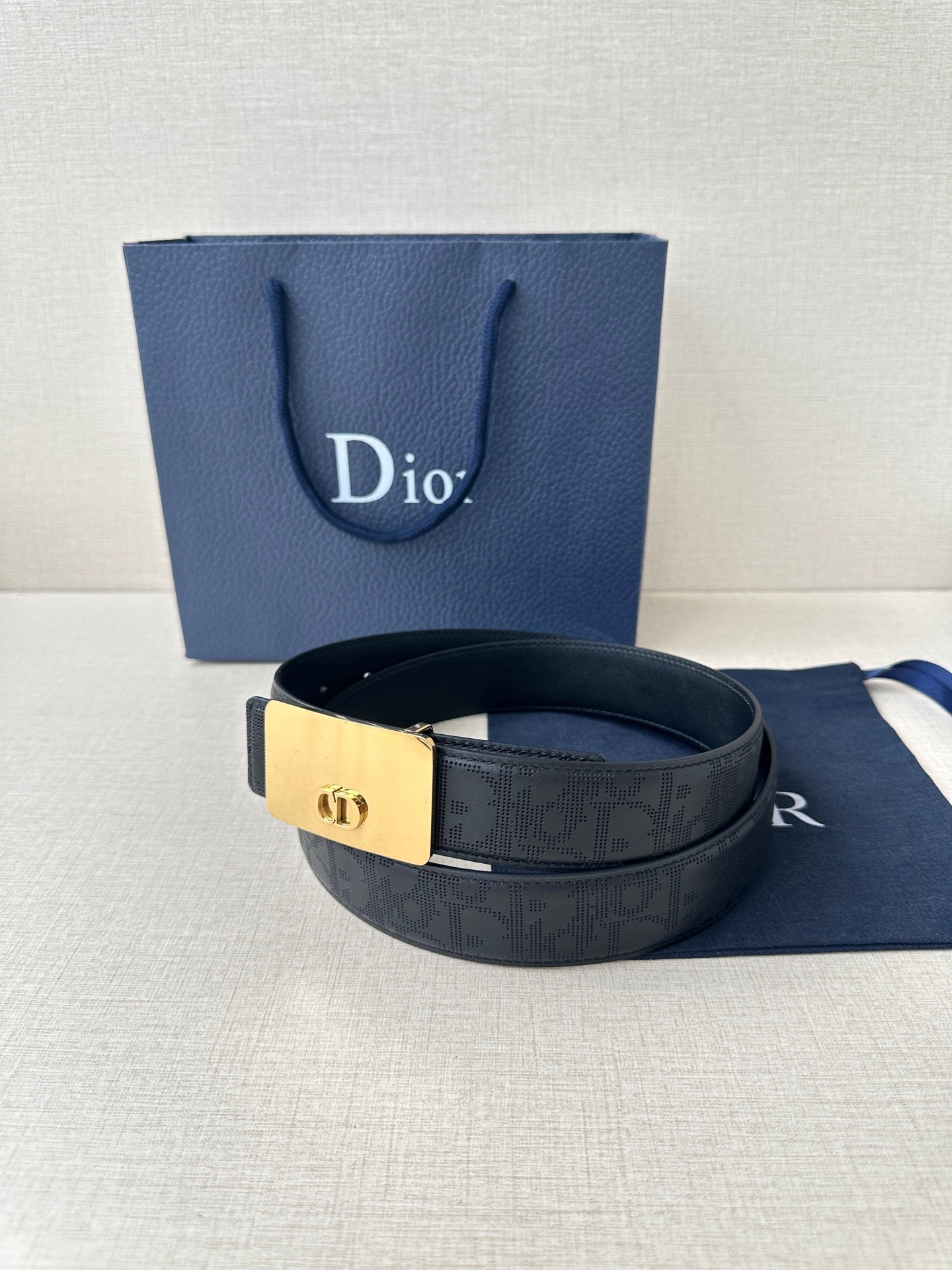 Dior belt with dark navy strap and gold-toned buckle, resting on a blue gift bag
