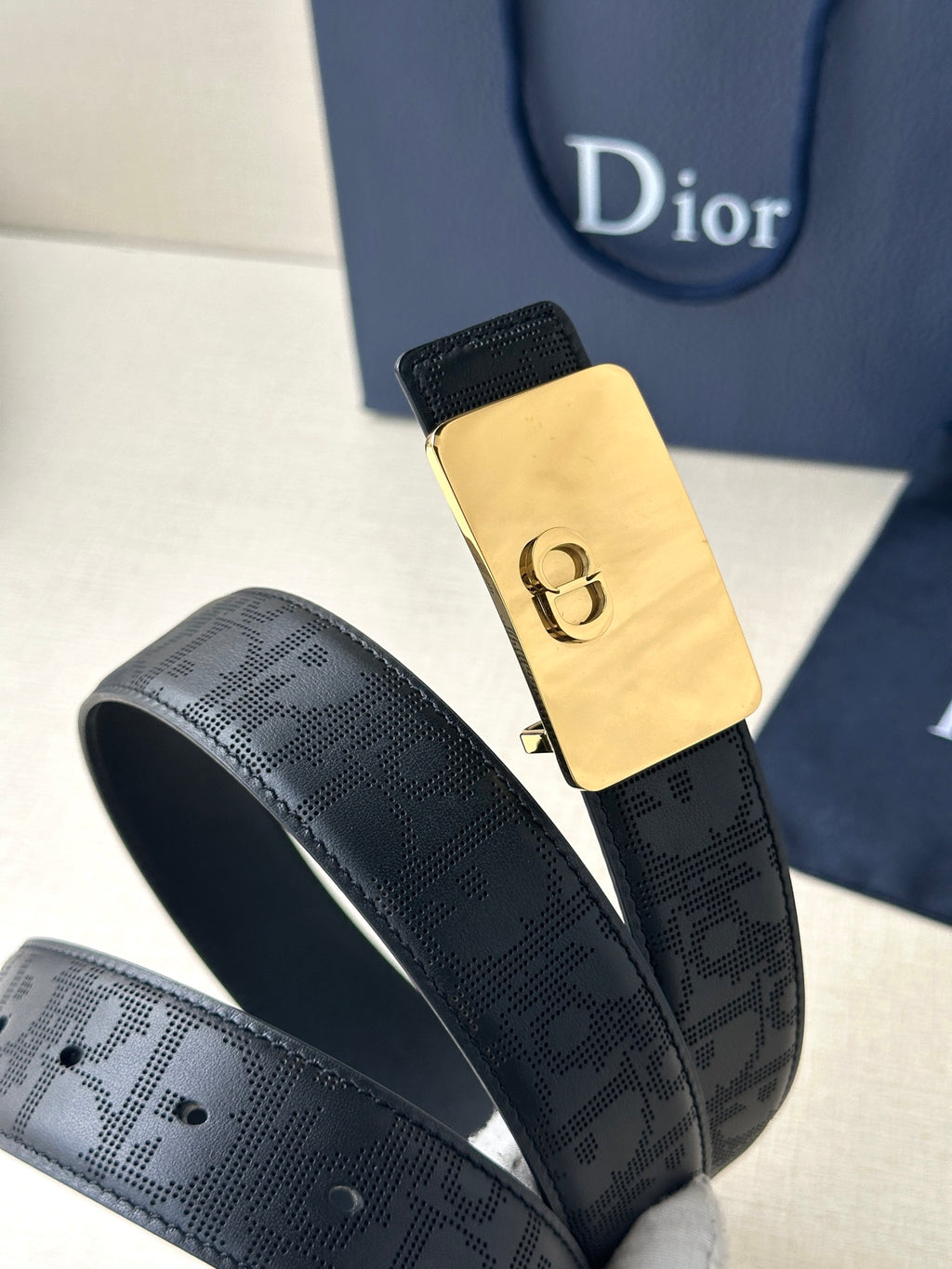 Dior belt detail view with embossed dark navy strap and gold-toned buckle plate