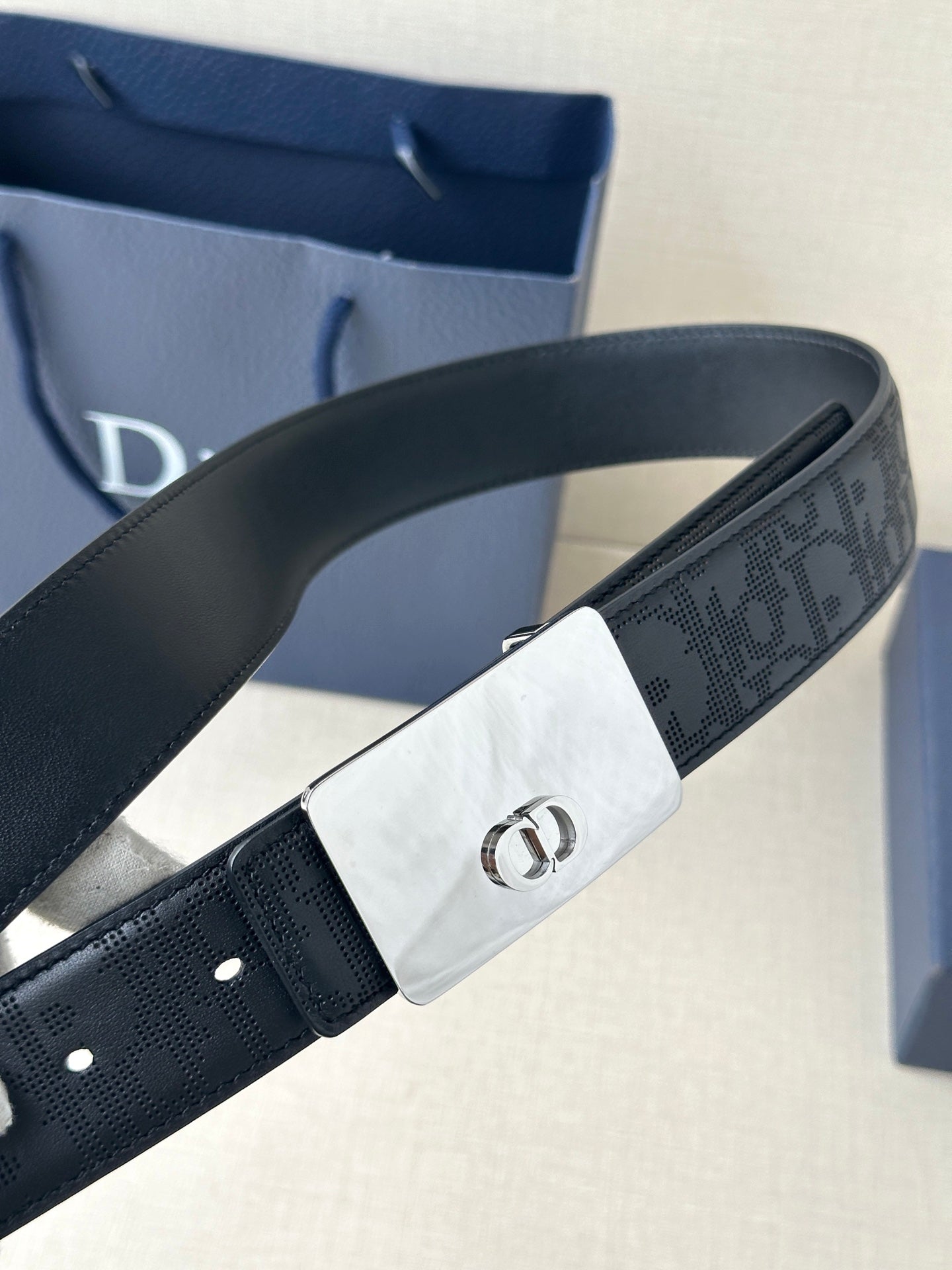 Dior belt close-up with dark navy logo-embossed strap and rectangular silver-toned buckle