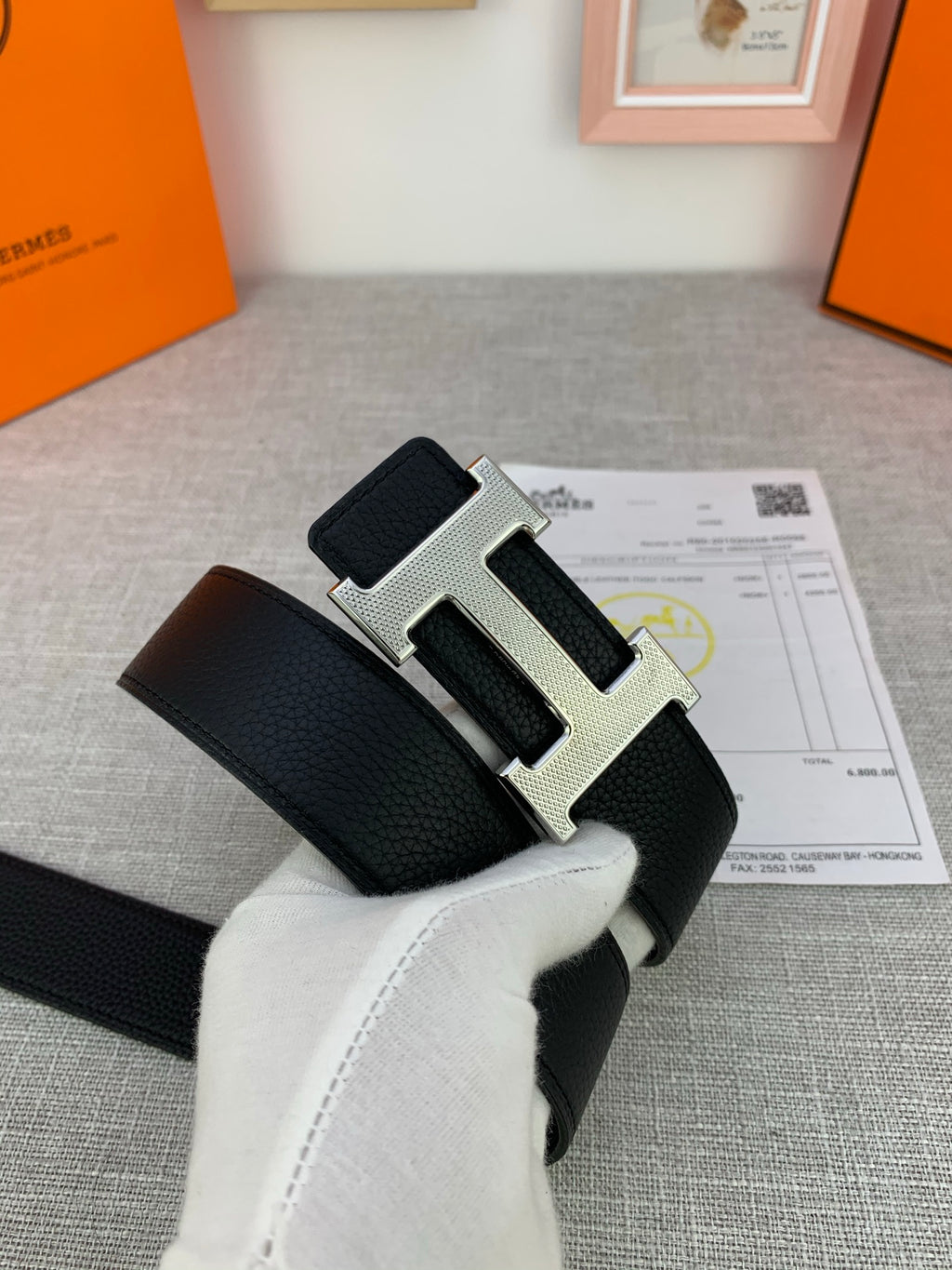 Black Hermes belt with gold H buckle on textured leather strap, held in glove