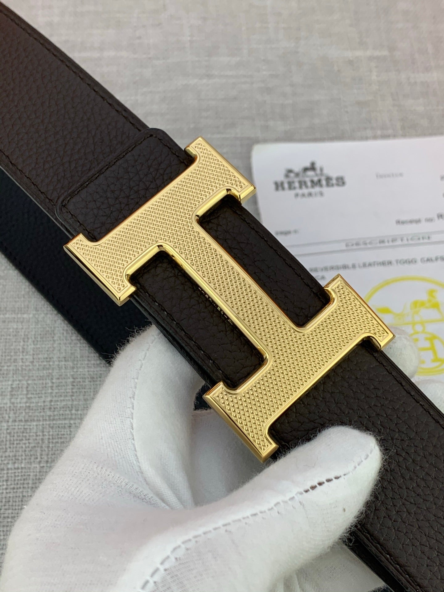 Close-up of gold-tone H buckle on dark leather belt