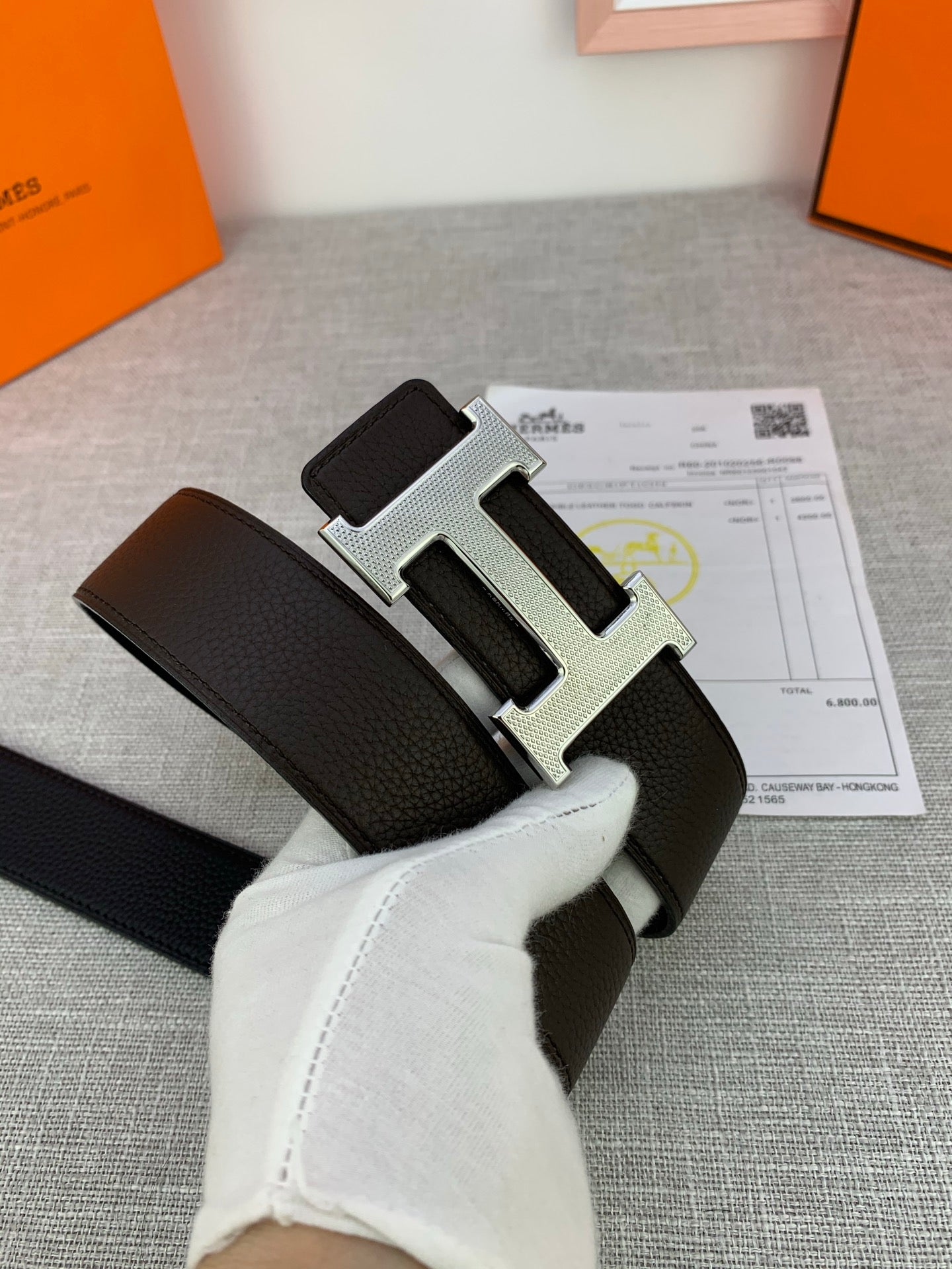 Dark leather belt with silver-tone H buckle, angled view