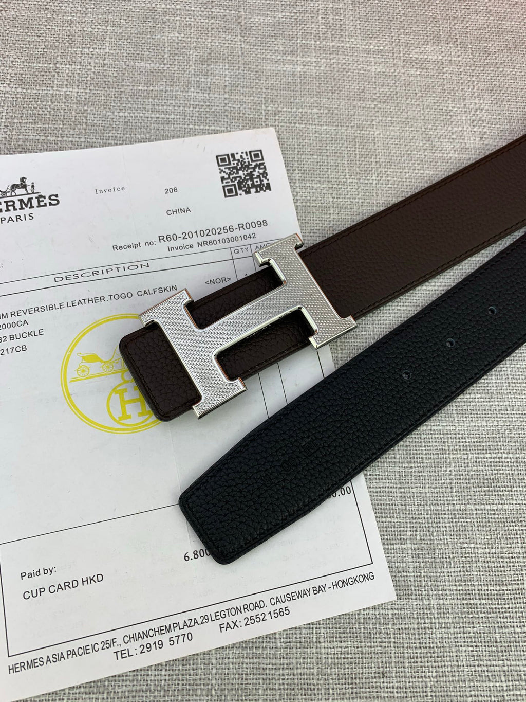 Close-up of dark leather belt end with silver-tone H buckle on paperwork