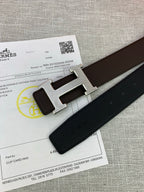 Close-up of dark leather belt end with silver-tone H buckle on paperwork