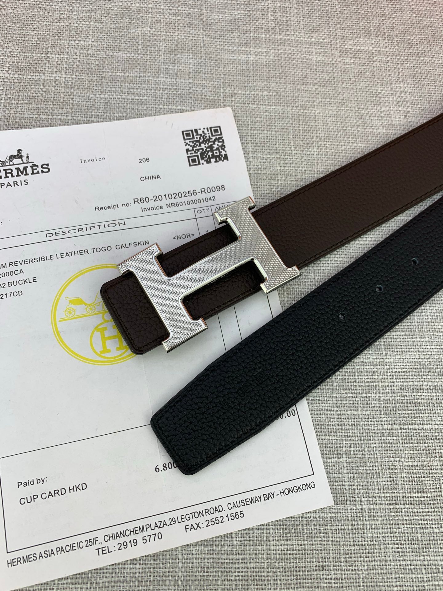 Close-up of dark leather belt end with silver-tone H buckle on paperwork