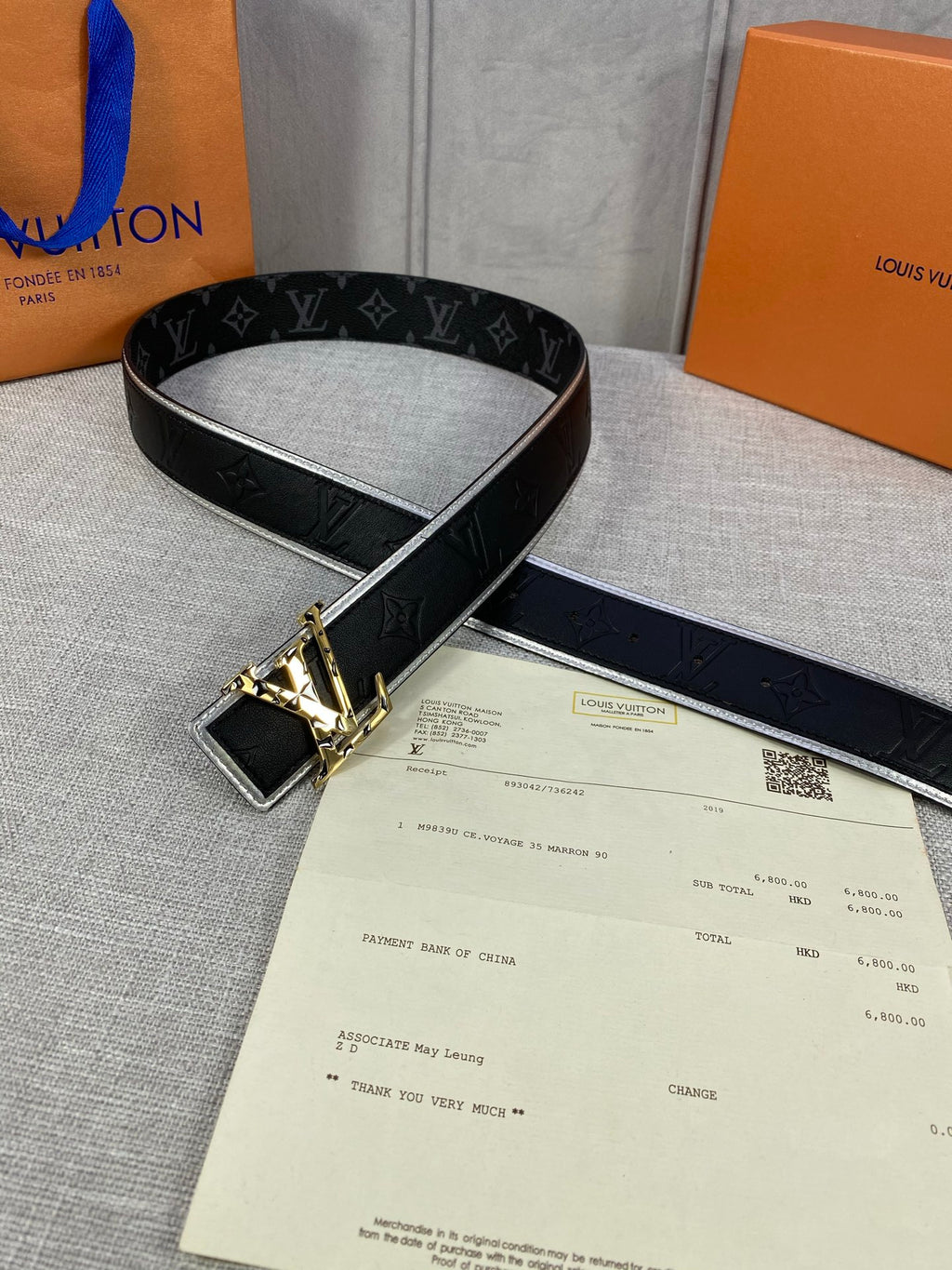 Black monogram belt with gold-tone square buckle, laid across a receipt