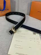 Black monogram belt with gold-tone square buckle, laid across a receipt