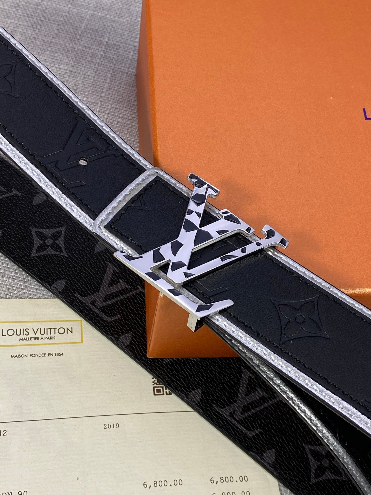 Black monogram belt close-up with silver-toned buckle and gold hardware