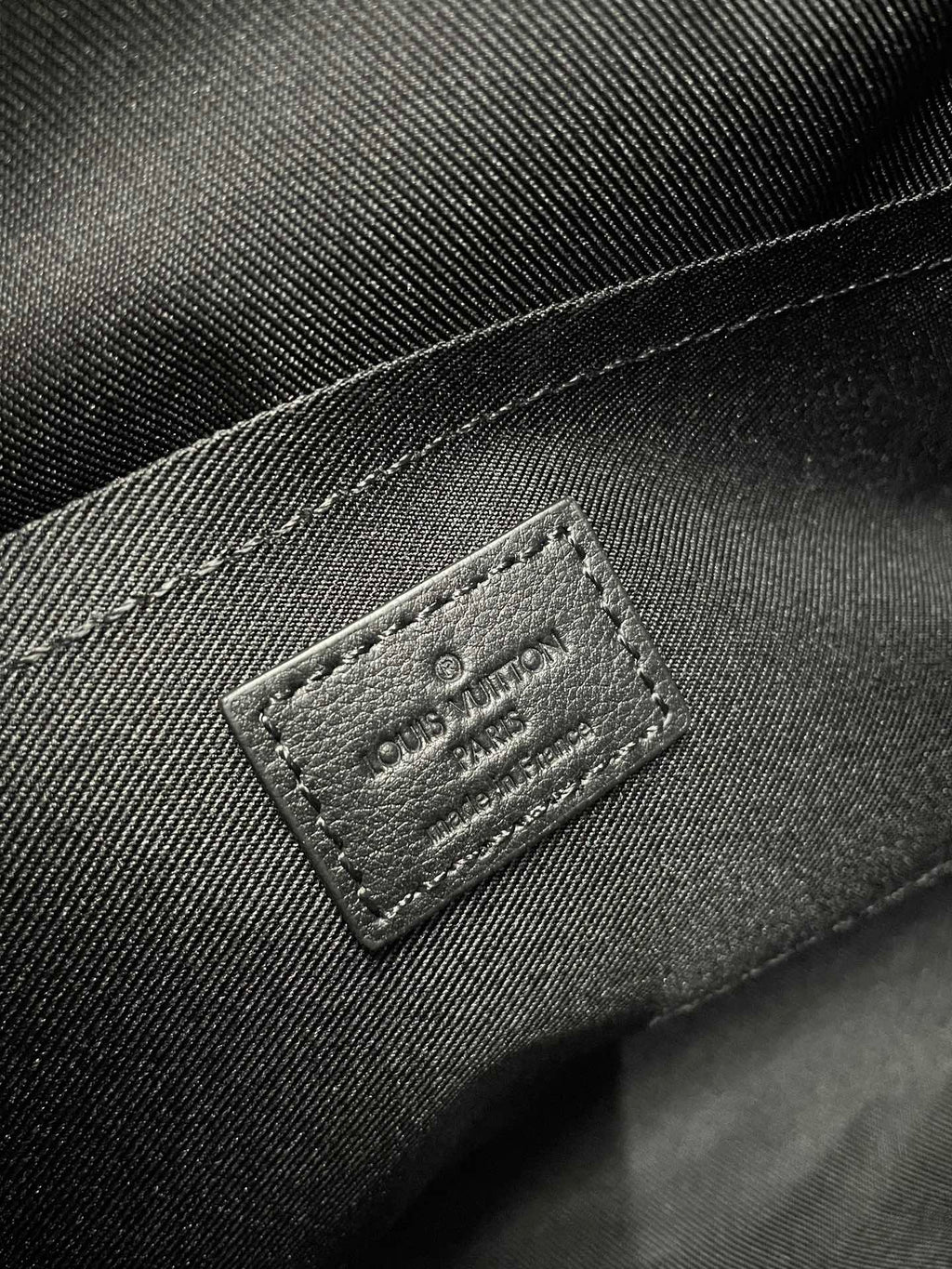 Men's Louis Vuitton bag label patch on dark fabric, stitched border and embossed logo