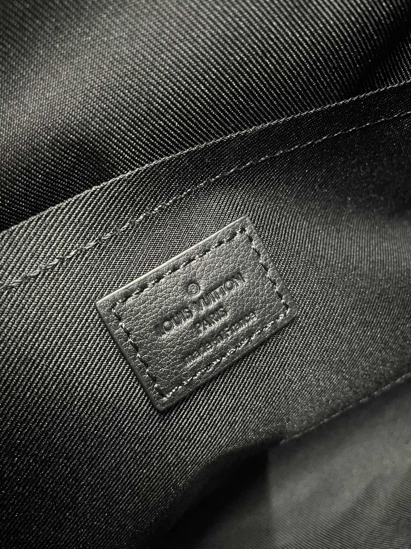 Louis Vuitton dark crossbody bag close-up of stitched logo leather label
