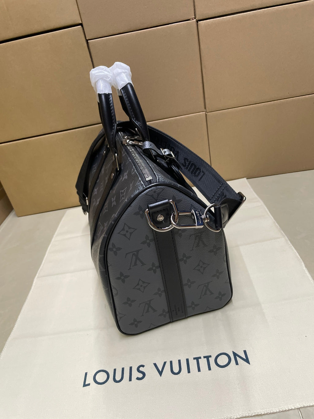 Louis Vuitton monogram duffel bag on side view with front buckle strap, dark gray