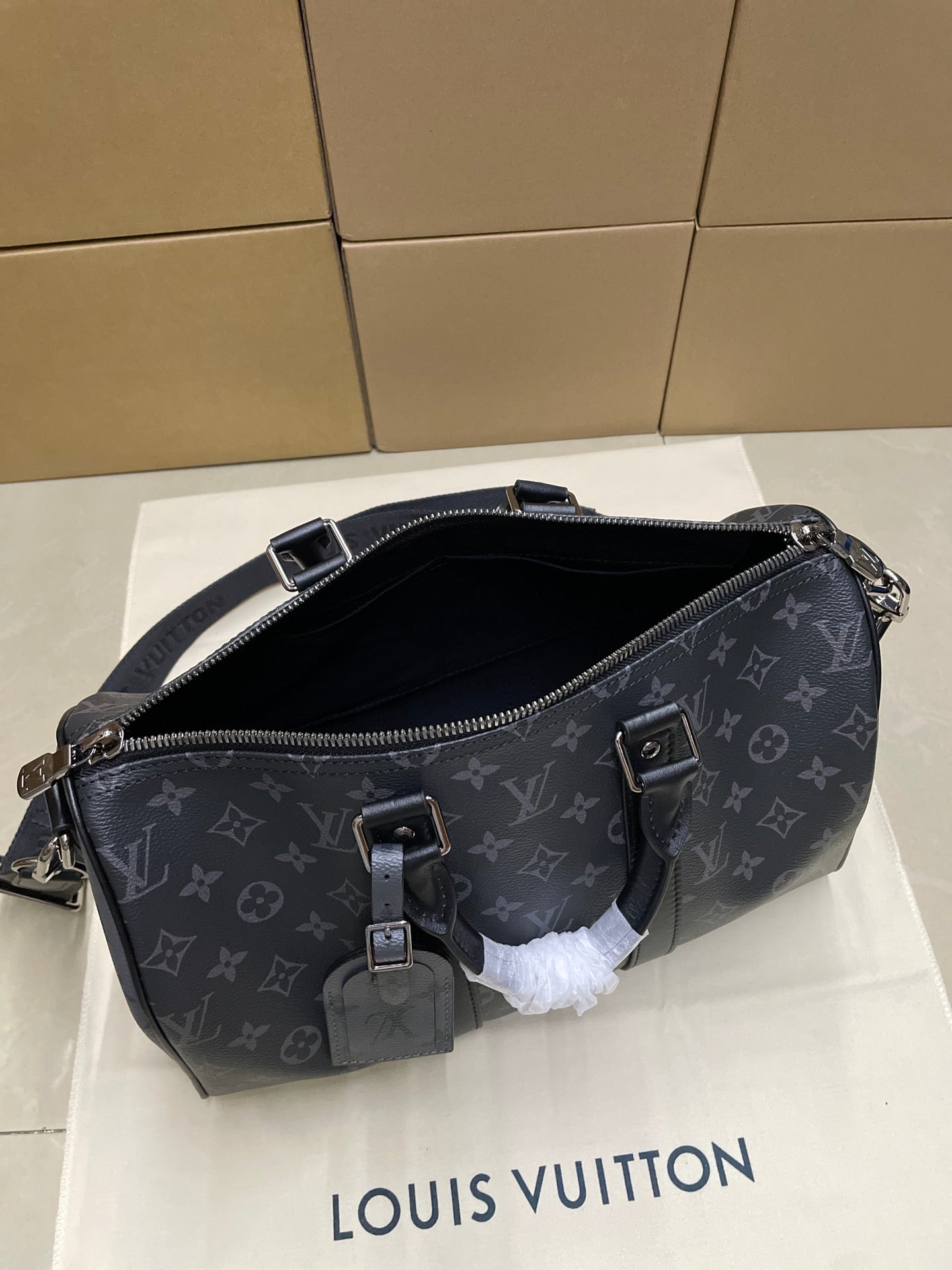 Monogram crossbody bag with open top, zipper pull, and front buckle detail