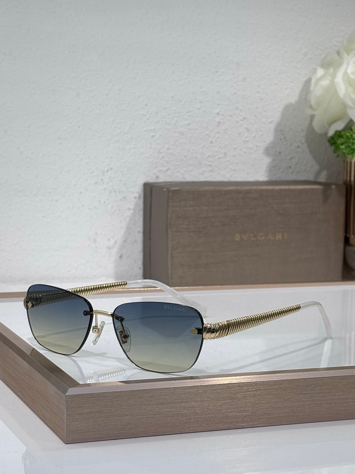 Metal-framed oval sunglasses with blue-green lenses and textured gold temples