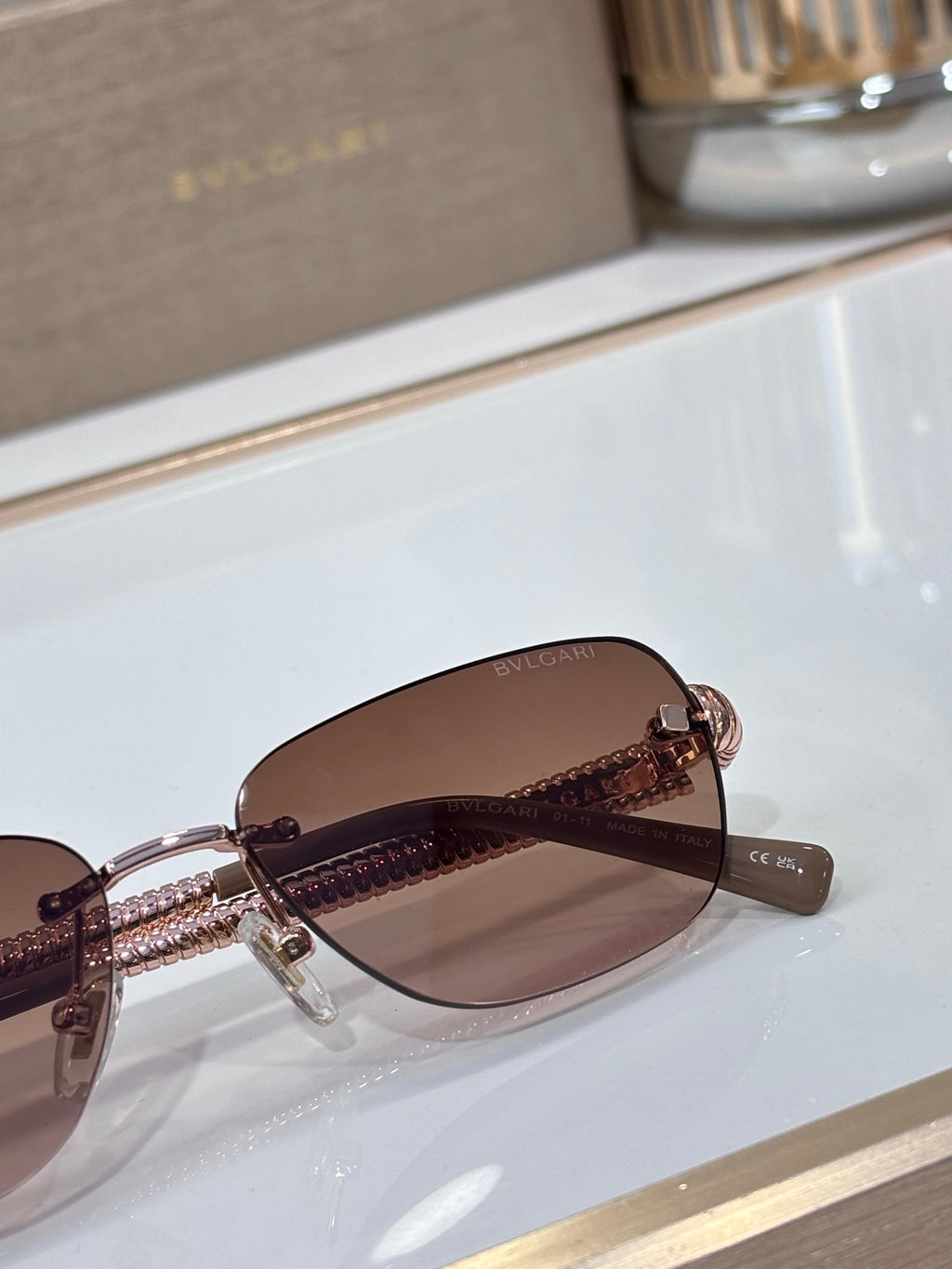 Brown-lensed oval sunglasses with metal frame and textured gold temple detail