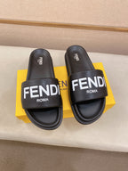 Pair of black slide sandals with wide strap and FENDI ROMA logo on the footbed.