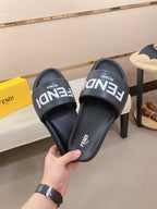 Black slide sandals held in hand, showing FENDI logo on the footbeds.