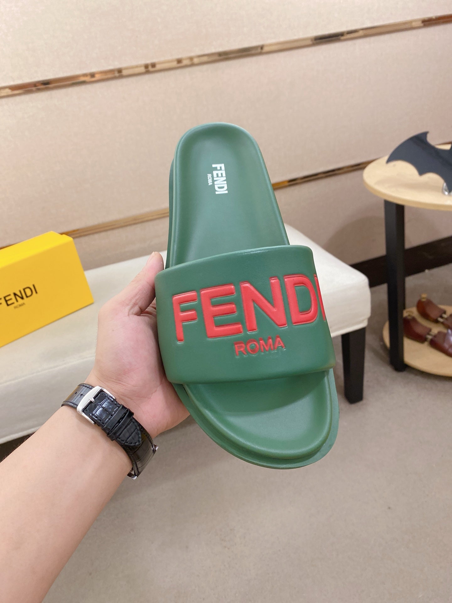 Green slide sandal held in hand, showing red FENDI logo on the strap and footbed.