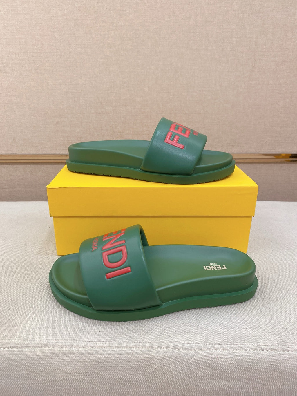 Green slide sandals on a yellow box, one sandal stacked over the other.