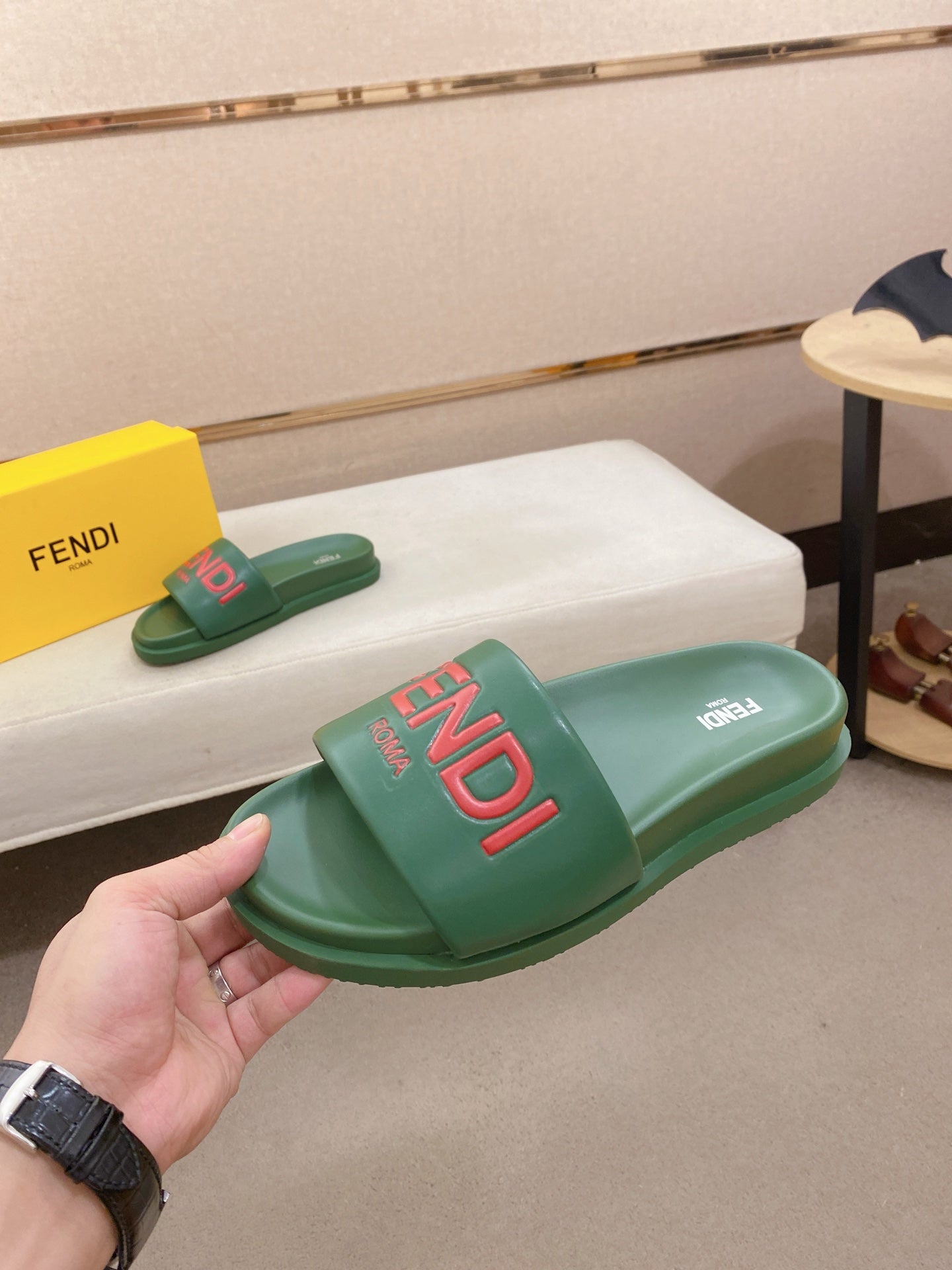 Green FENDI slide sandal held at an angle, with red logo printed on the footbed.