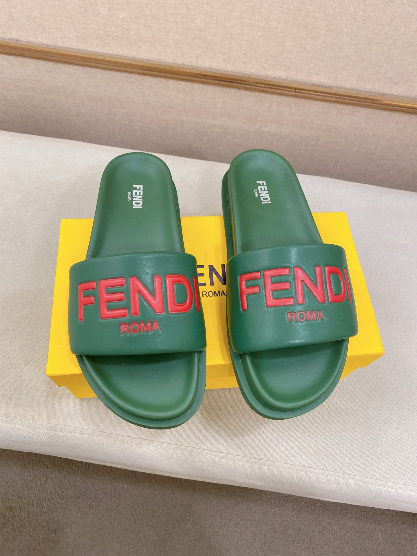Two green FENDI slide sandals with red FENDI logo on the front straps.