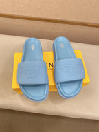 Light blue slide sandals side-by-side on yellow box, showing embossed branding on each
