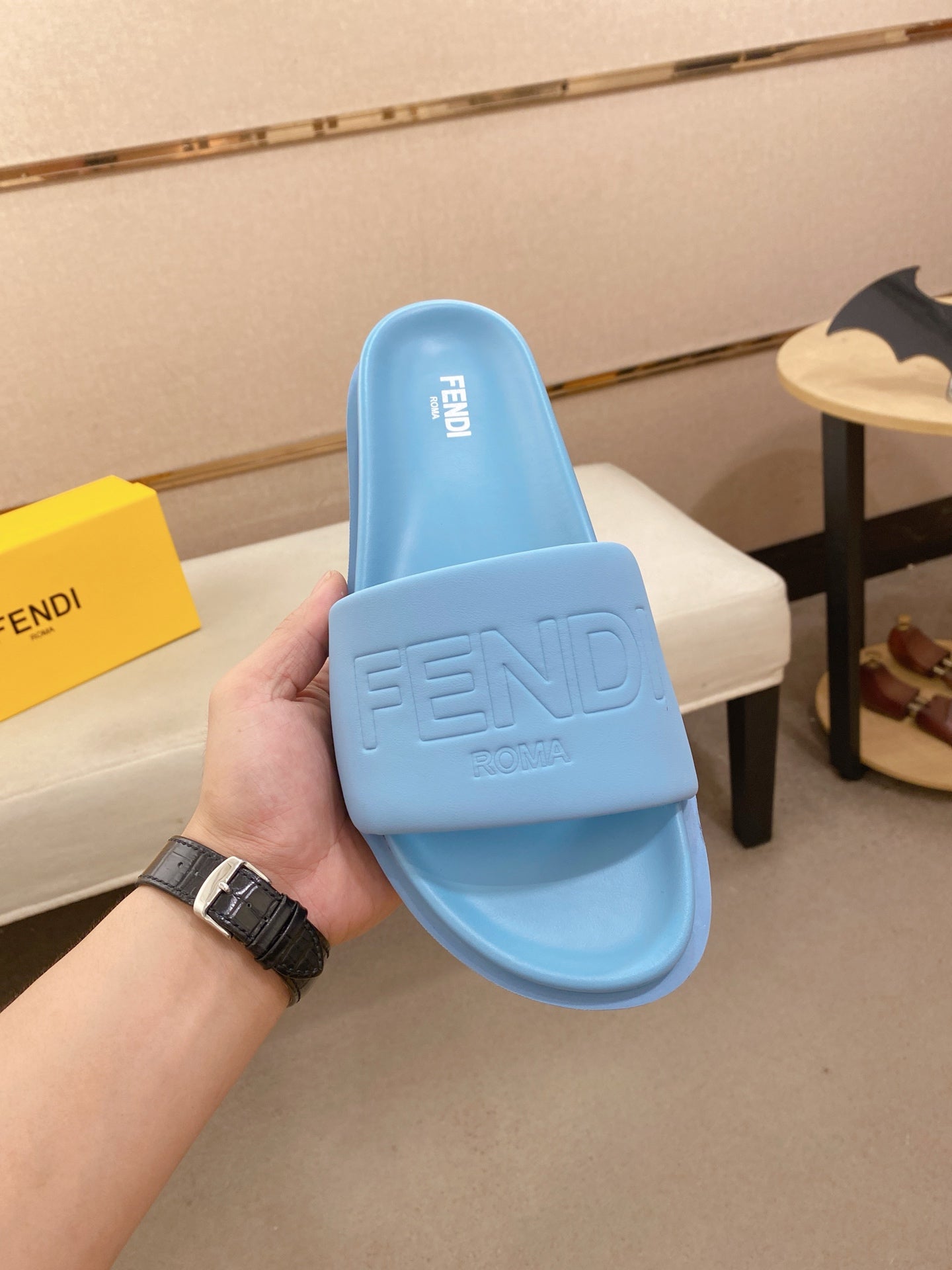 Light blue slide sandals held by hand, showing front strap with embossed Fendi logo