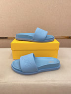 Light blue slide sandals on yellow box, top view with embossed logo on footbed