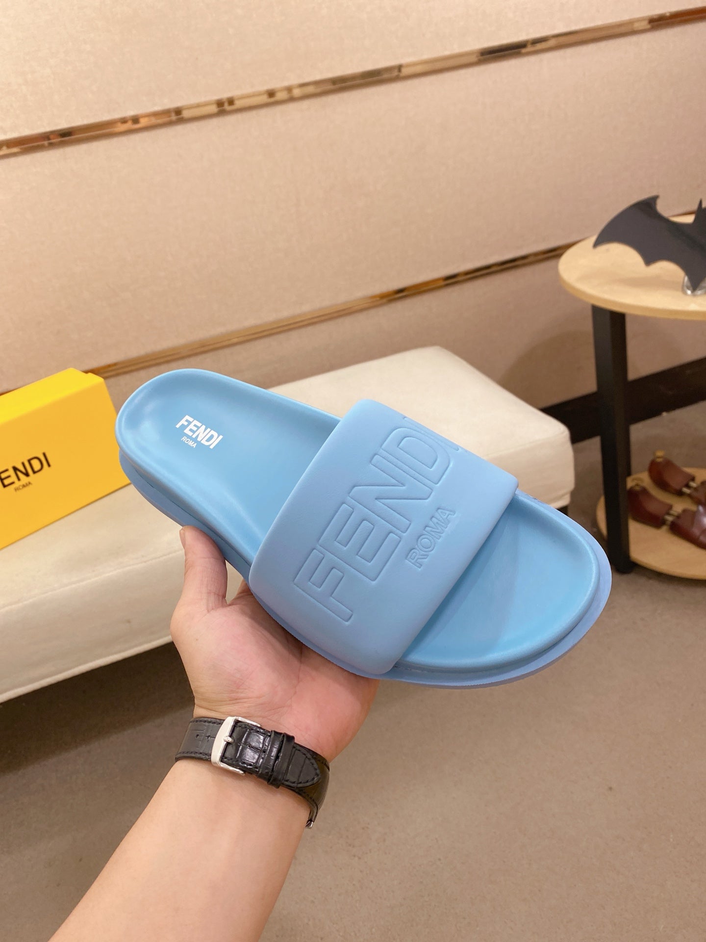 Light blue slide sandals held up, featuring embossed logo on strap and front footbed