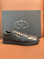 Dark leather sneakers with gold-toned Prada logo and lace-up front.