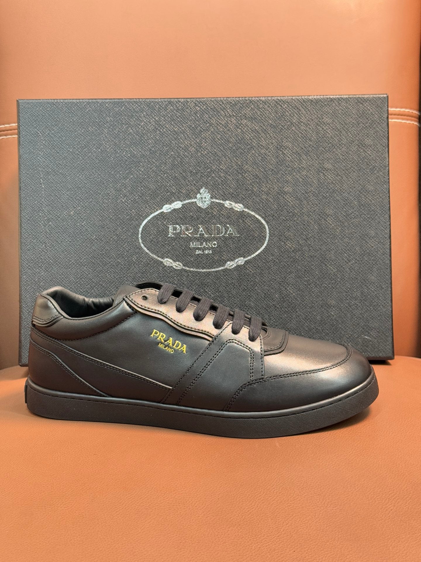 Dark leather sneakers with gold-toned Prada logo and lace-up front.