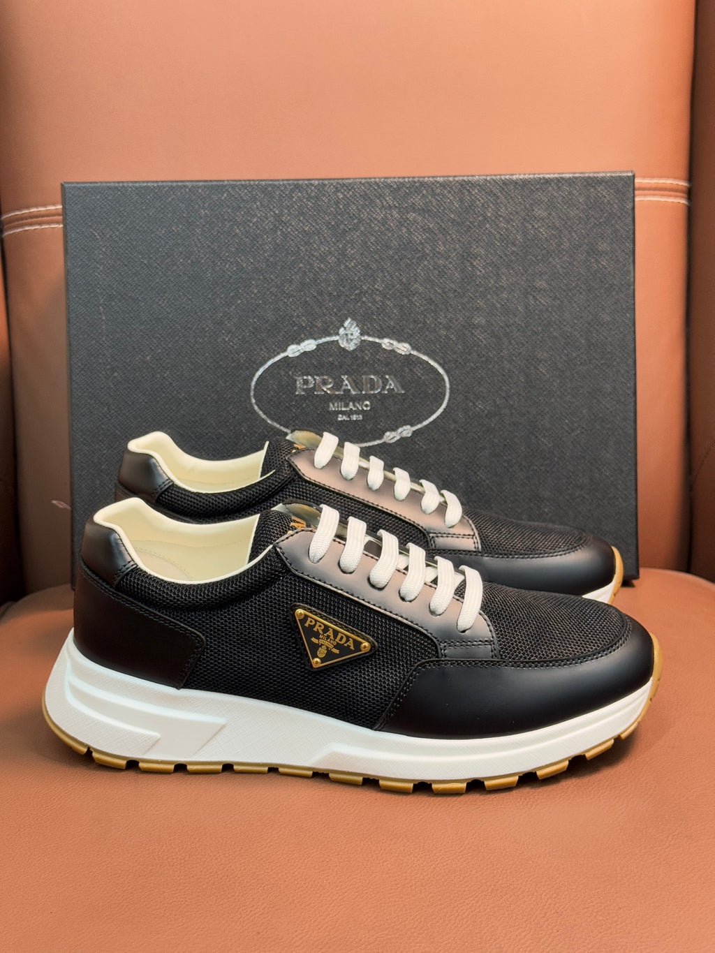 Prada unisex sneakers, dark mesh upper with beige accents, white laces, ridged outsole.