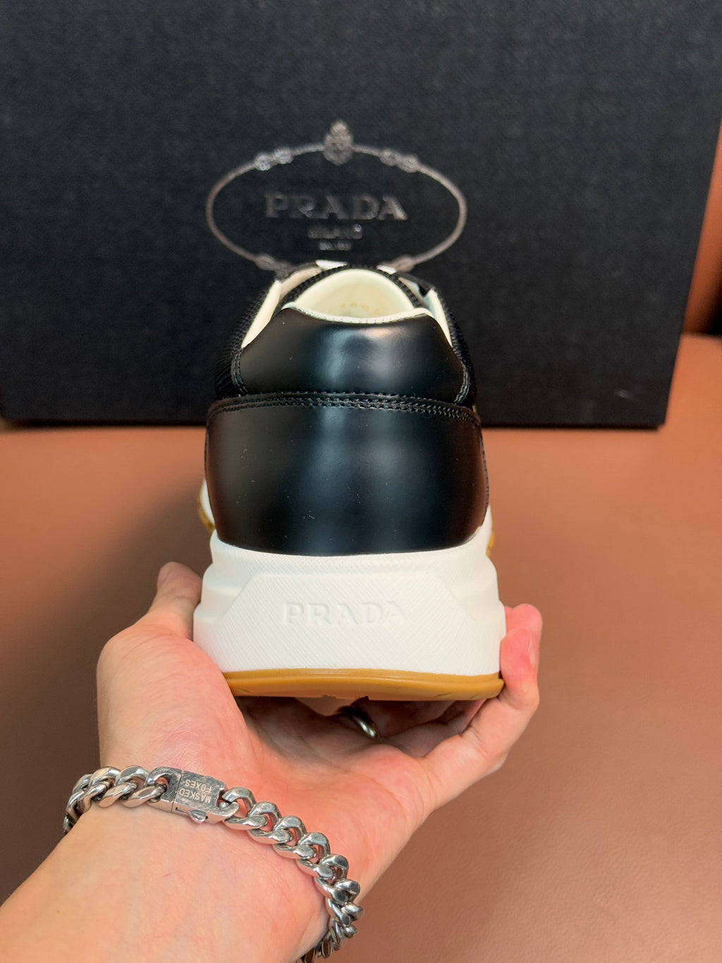 Prada unisex sneaker heel close-up, dark back, white midsole with logo.